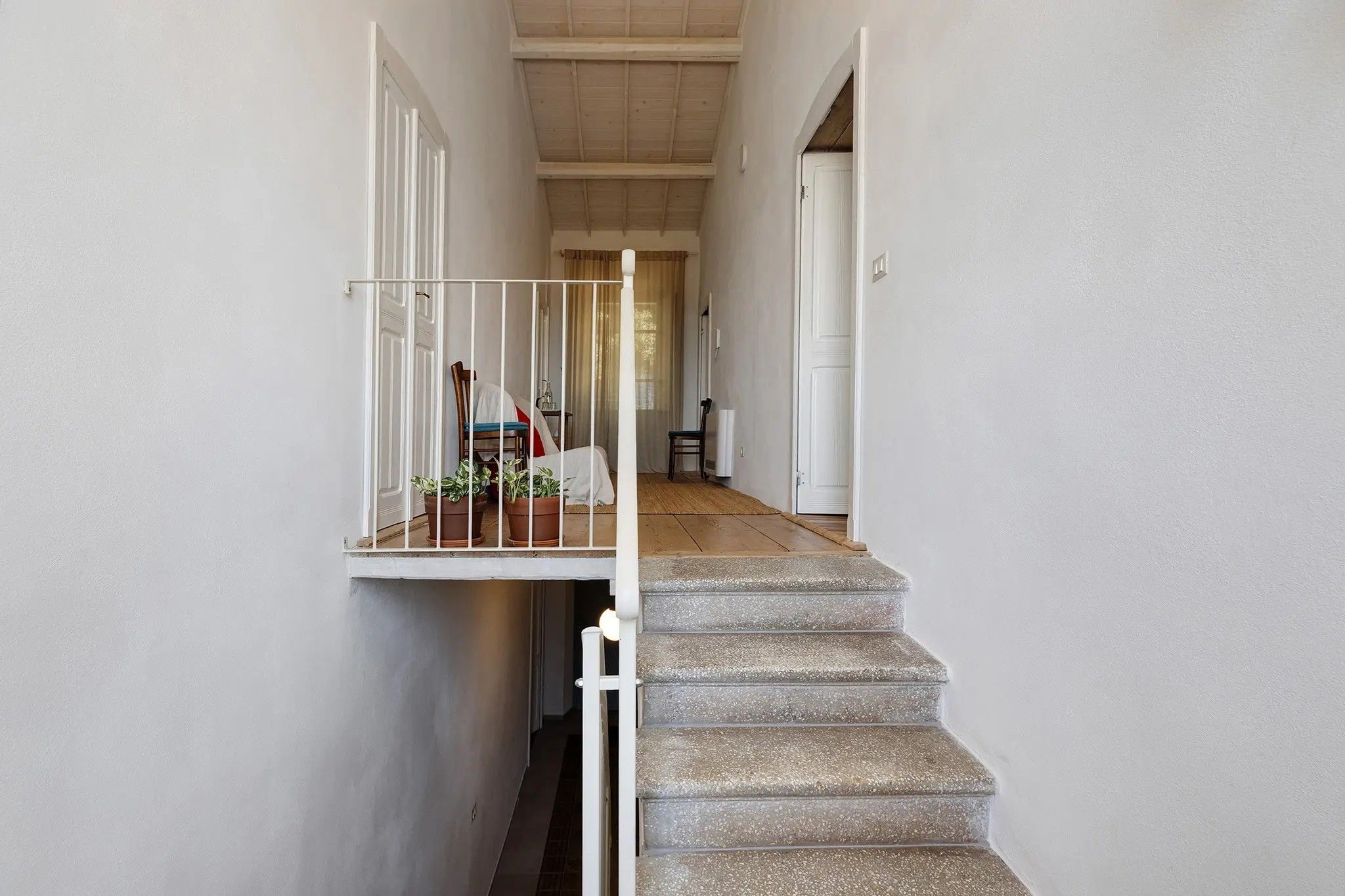 Una escalera con barandilla de metal que lleva a un rellano con una silla y plantas en macetas.