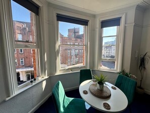 Una habitación con una mesa redonda, dos sillas y vistas a un paisaje urbano a través de amplios ventanales.