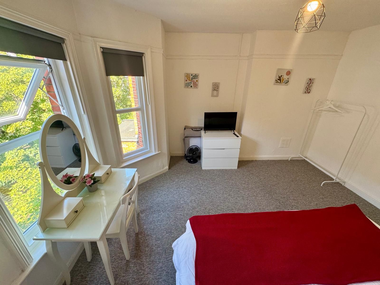 Een slaapkamer met een bed, een bureau met spiegel, een televisie en een radiator.