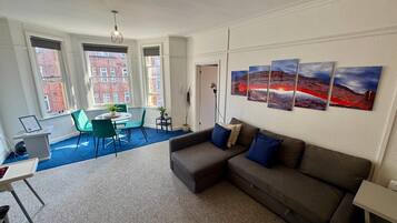 Een moderne woonkamer met een hoekbank, een eethoek met tafel en stoelen, en grote ramen met uitzicht over de stad.
