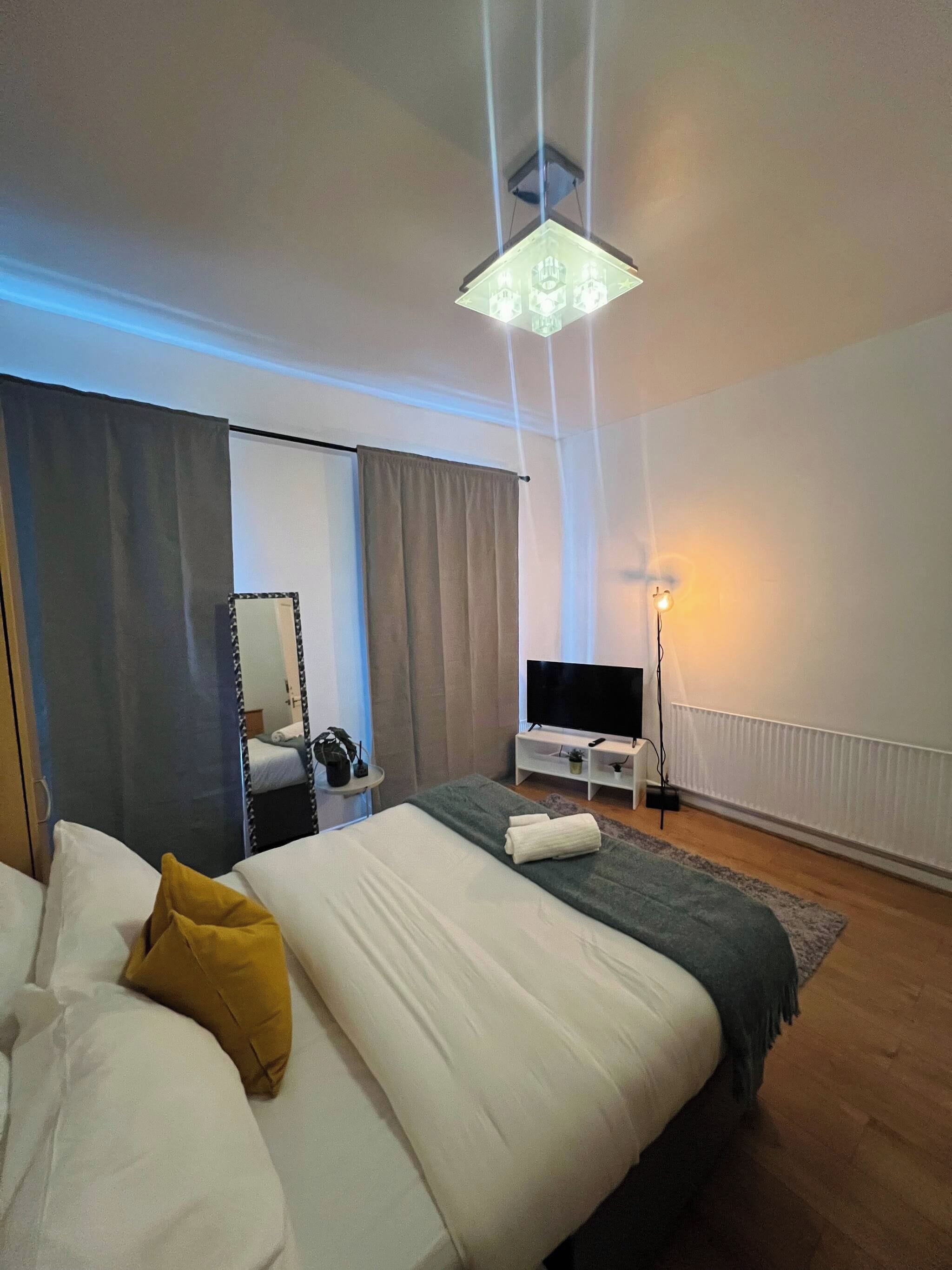 Une chambre d’hôtel moderne dotée d’un grand lit, d’une télévision à écran plat, d’une table de chevet avec une lampe et d’un grand miroir.