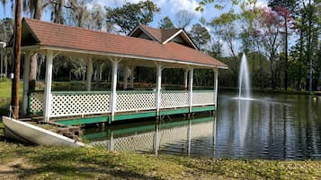 Ein überdachter Pavillon mit Dach und offenen Seiten, gelegen am Ufer eines ruhigen Sees mit einer Springbrunnen.