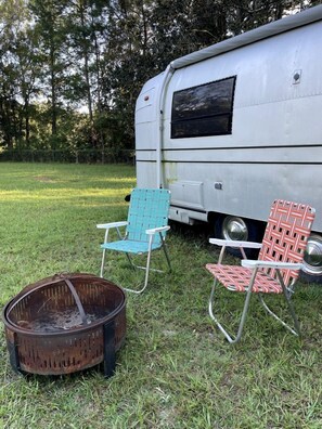 A white RV parked on grass with two chairs and a metal bucket.