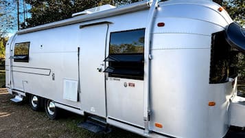 A silver RV with a sliding door, a small window, and a step leading to the entrance.