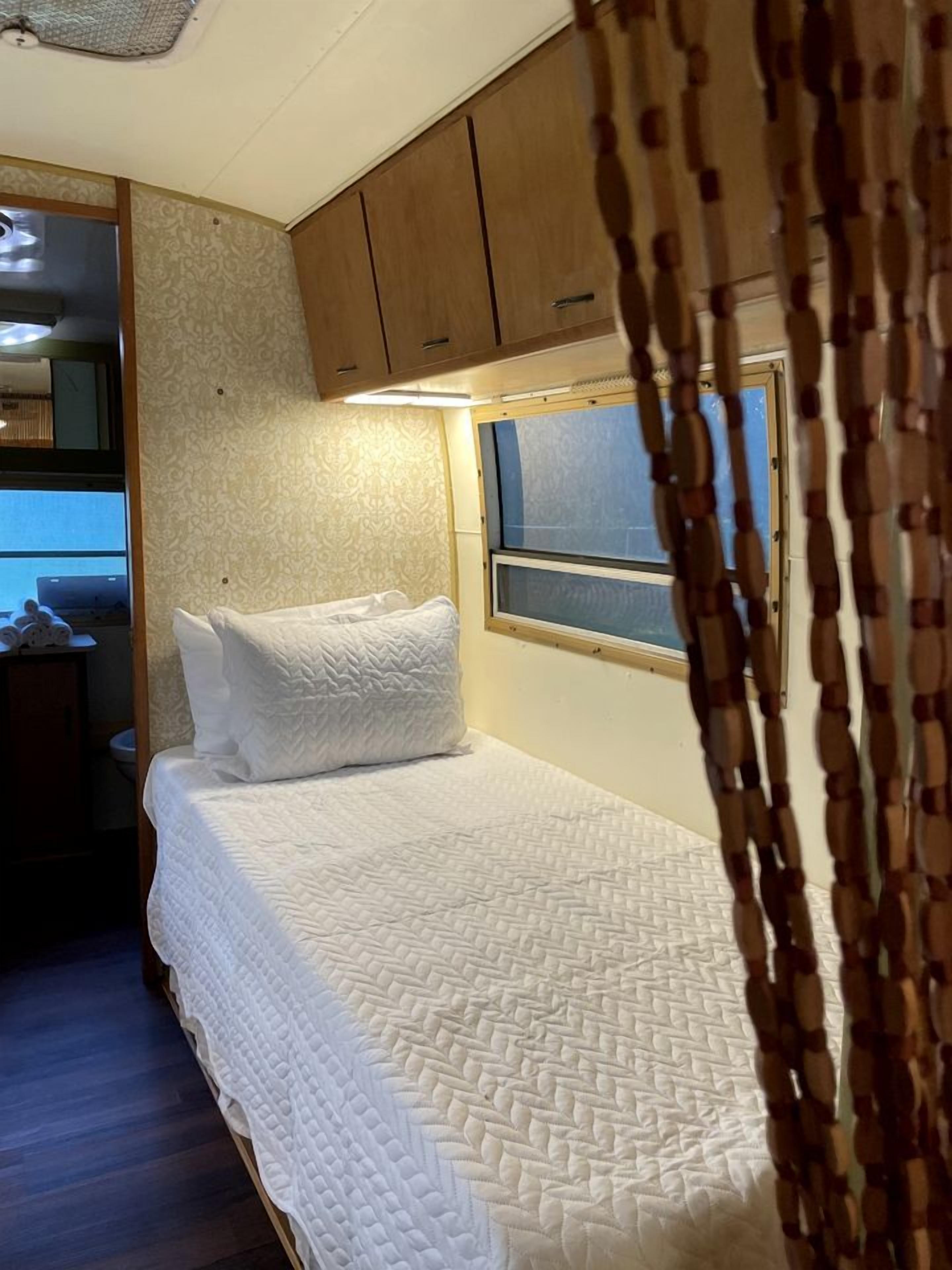 Un lit recouvert d’une courtepointe matelassée, des armoires en bois et une fenêtre avec des stores.