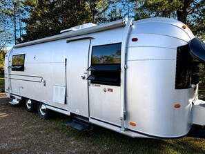 A silver RV with a sliding door, a small window, and a step leading to the entrance.