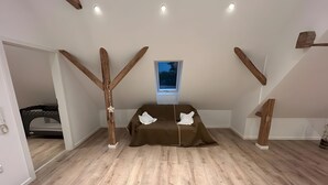 Ein Zimmer mit schrägem Dach, Holzbalken, einem Etagenbett, einem braunen Sofa und einem Fenster mit Aussicht.