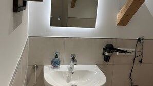 Ein Badezimmer mit einem weißen Waschbecken, einem Spiegel, einem Handtuchhalter und einer Seifenspenderflasche.