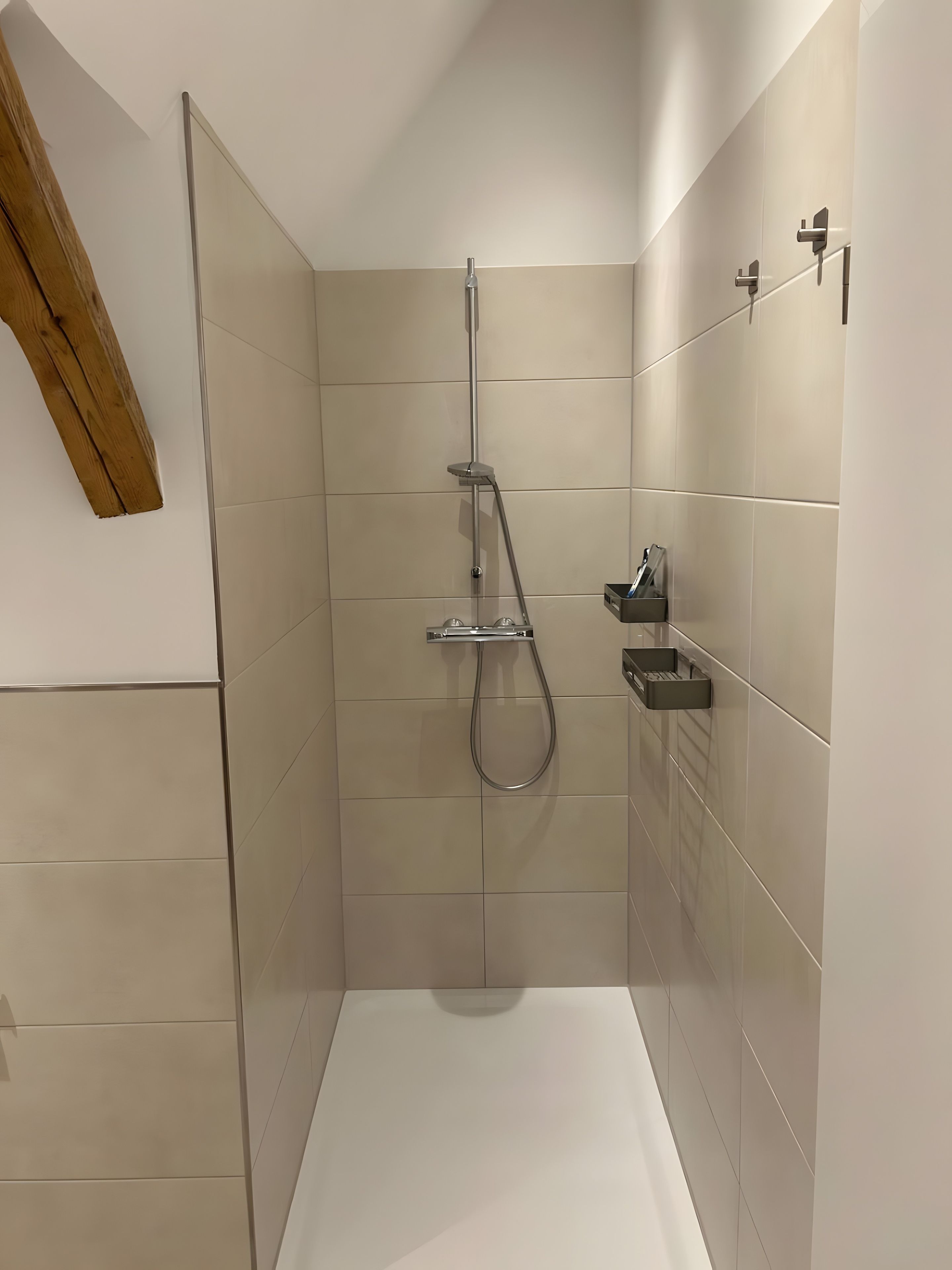 En modern dusch med ett duschmunstycke som kan hållas i handen, en väggmonterad blandare och en liten hylla för toalettartiklar.