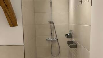 En modern dusch med ett duschmunstycke som kan hållas i handen, en väggmonterad blandare och en liten hylla för toalettartiklar.