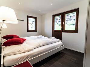 Une chambre à coucher avec un lit, une table de chevet, une lampe et deux fenêtres.
