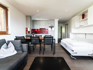 Un espace de vie moderne et compact comprenant un coin cuisine, un espace repas et un lit.