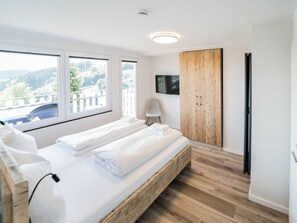 A modern bedroom with a large bed, a wooden wardrobe, a television, and a view of the outdoors. - Holiday Apartment 712 (Winterberg)