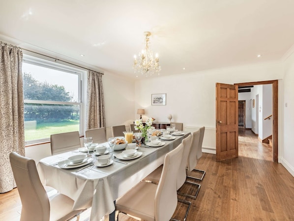 A dining room with a table set for six, a chandelier, and a view of the outdoors.