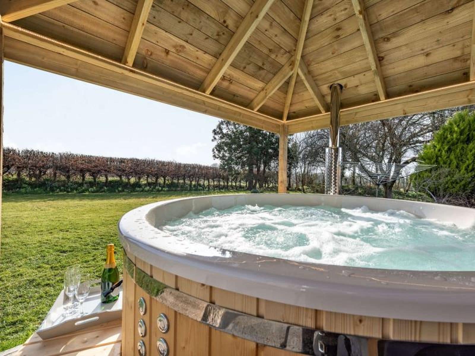 A hot tub under a wooden pergola with a vineyard in the background.