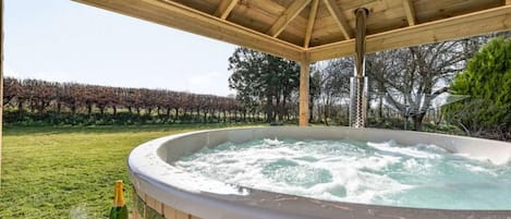 A hot tub under a wooden pergola with a vineyard in the background.