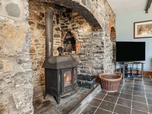 A stone fireplace with a black stove, a basket, and a television on the wall.