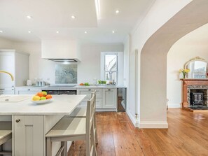 A modern kitchen with white cabinetry, a central island with fruit, and a stone fireplace.
