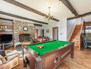 A room with a pool table, a fireplace, a television, and a staircase.