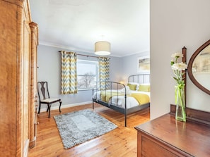 A bedroom with a bed, a chair, a wooden wardrobe, a mirror, and a window with curtains.