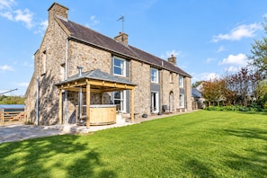 A stone house with a wooden deck and a hot tub.