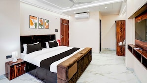 A modern bedroom with a bed, bedside tables, a bench, a ceiling fan, an air conditioner, and a wooden wardrobe. - Townhouse Khajrana Ganpati Mandir (Indore)