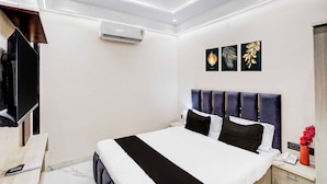 A modern hotel room with a large bed, a flat-screen TV, an air conditioning unit, and a bedside table with a lamp and a vase of flowers. - Townhouse Khajrana Ganpati Mandir (Indore)