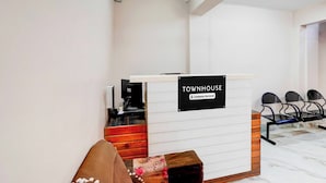 A reception desk with a sign indicating it is a company-serviced townhouse. There are chairs and a small table with a vase of flowers. - Townhouse Khajrana Ganpati Mandir (Indore)