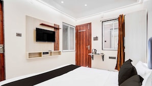 A modern hotel room with a large bed, a flat-screen TV mounted on the wall, a wooden door, and a window with curtains. - Townhouse Khajrana Ganpati Mandir (Indore)