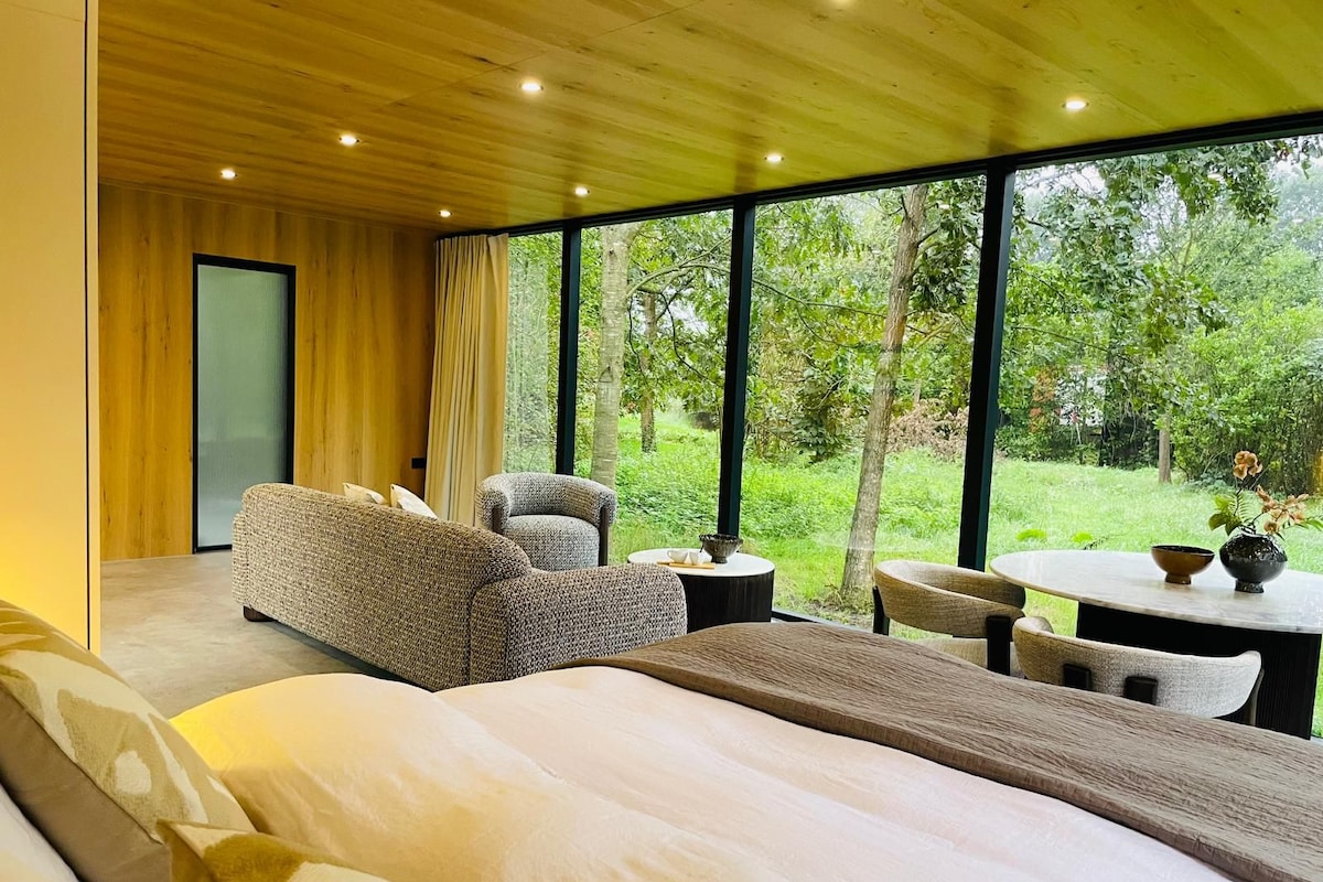 A modern bedroom with a large bed, a sofa, a chair, and a table with a vase.