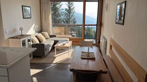 A modern living room with a sofa, a dining table, and a view of mountains through large windows. - Apartment in Les Arcs 1800 for 8 people (Bourg-Saint-Maurice)