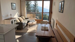 Uma sala de estar moderna com sofá, mesa de jantar e vista para montanhas através de grandes janelas.