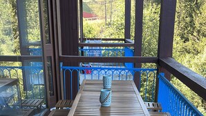 An outdoor wooden deck with a table and benches, a blue railing, and a view of trees and a building in the background. - Apartment in Les Arcs 1800 for 8 people (Bourg-Saint-Maurice)