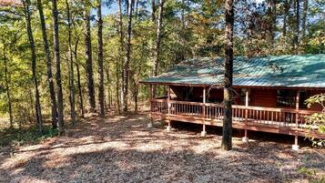 A cabin with a wooden deck and a metal roof, surrounded by a forest.
