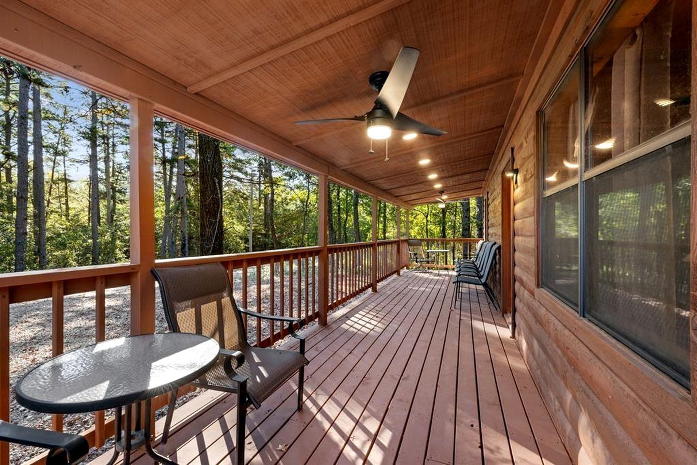 Eine überdachte Terrasse im Freien mit Tisch und Stühlen, umgeben von Holzgeländern und großen Fenstern.