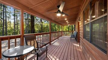 Eine überdachte Terrasse im Freien mit Tisch und Stühlen, umgeben von Holzgeländern und großen Fenstern.