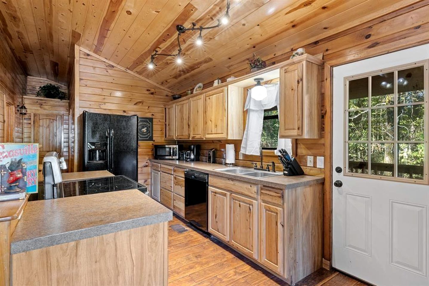 Ein Interieur einer Holzhütte mit einer Küche, ausgestattet mit Kühlschrank, Mikrowelle, Spüle und Holzschränken.