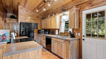 Ein Interieur einer Holzhütte mit einer Küche, ausgestattet mit Kühlschrank, Mikrowelle, Spüle und Holzschränken.