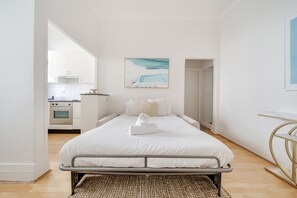Ein Schlafzimmer mit einem Bett, einem Gemälde und Blick zur Küche.