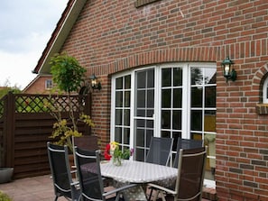 Ein Backsteinhaus mit einem weiß gefassten Fenster, einem Tisch mit Stühlen und einem Blumentopf.