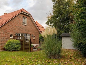 Ein Ziegelhaus mit rotem Ziegeldach, einem Holztor und einem kleinen Garten mit Gras und Bäumen.