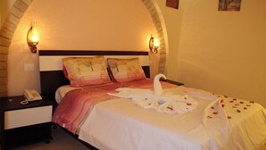 A hotel room with a brick archway, a bed with a white bedspread, two pillows, a telephone on a nightstand, and wall sconces. - Offra Douz  (Ghlissia)