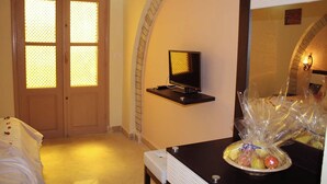 A hotel room with a bed, a television on a stand, and a wall-mounted shelf with a basket of fruit. - Offra Douz  (Ghlissia)