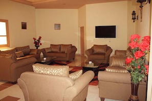 A living room with sofas, a coffee table, and a flat-screen TV mounted on the wall.