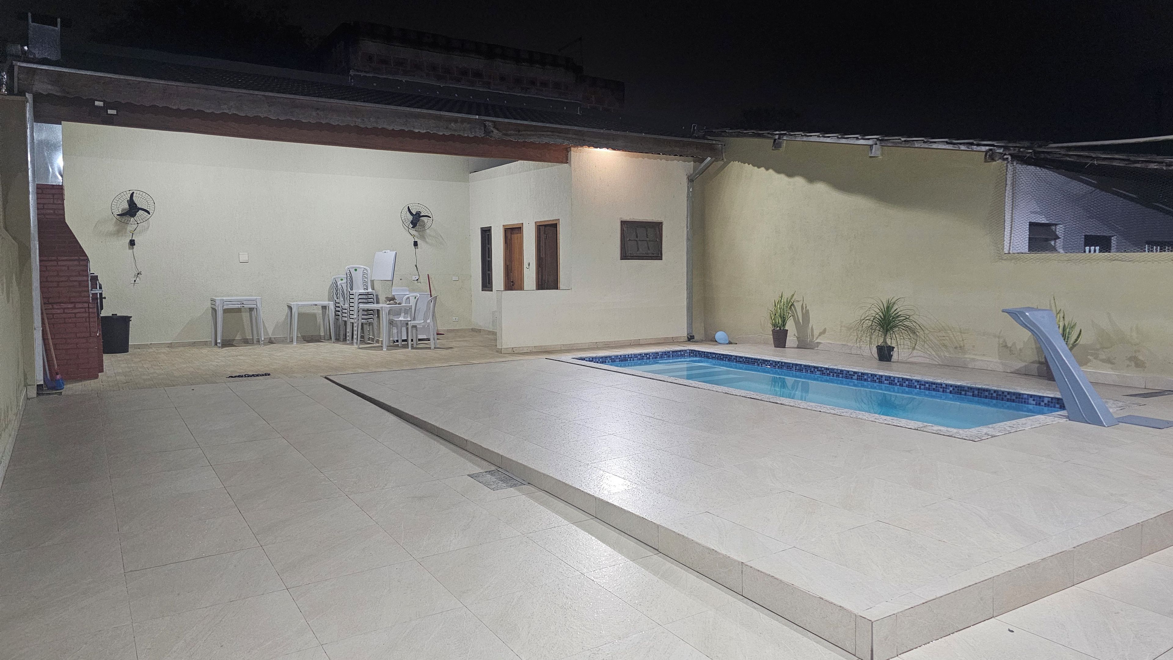 A swimming pool with a tiled deck, a small table with chairs, and a few potted plants.