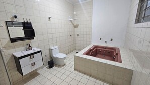 A bathroom with a white toilet, a sink with a mirror, and a bathtub. - House for 6. Private pool | Hot tub (Pindamonhangaba)