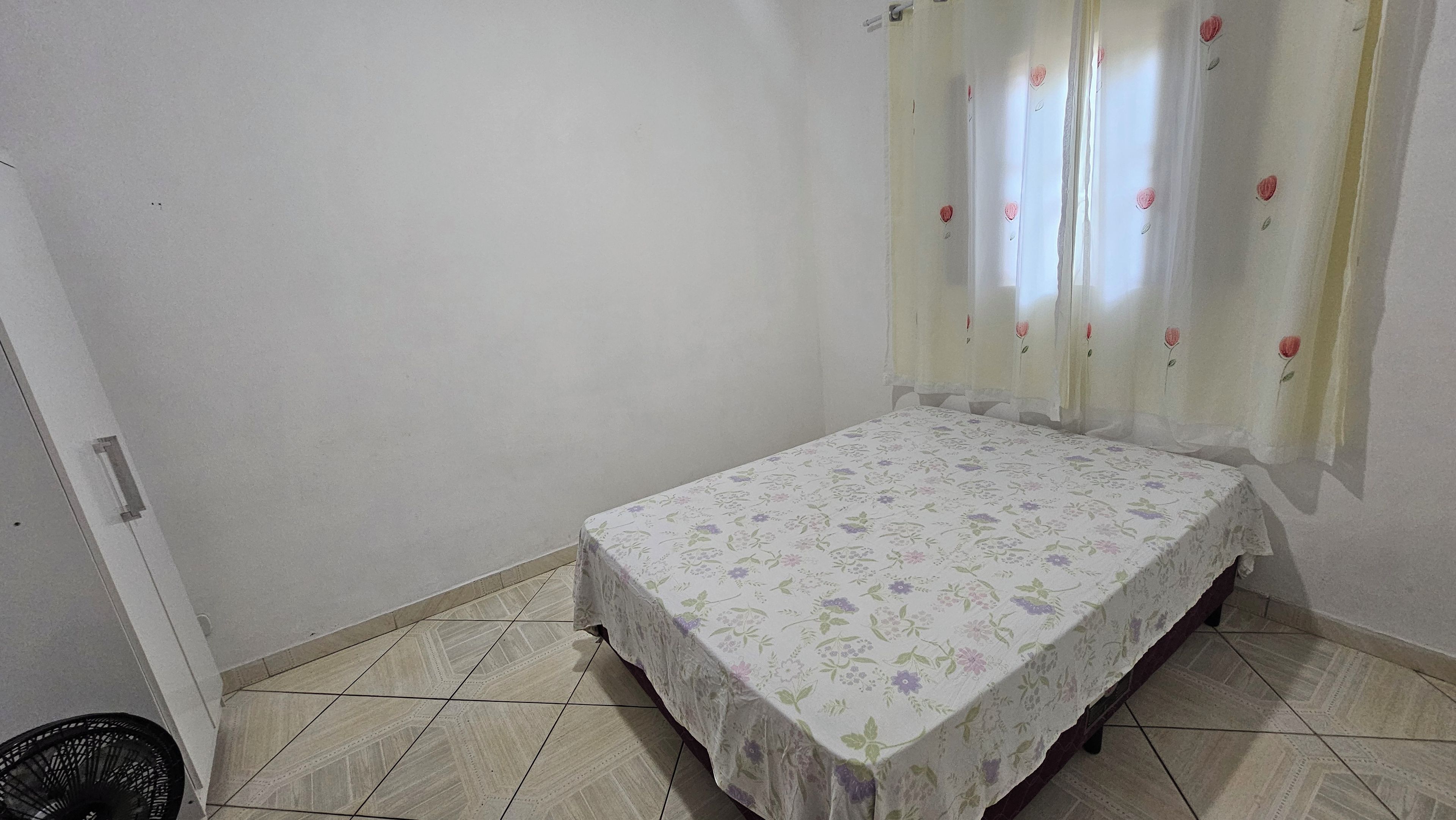 Una habitación pequeña con cama individual, colcha estampada, paredes lisas y suelo de baldosas.