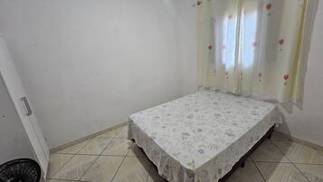 Una habitación pequeña con cama individual, colcha estampada, paredes lisas y suelo de baldosas.