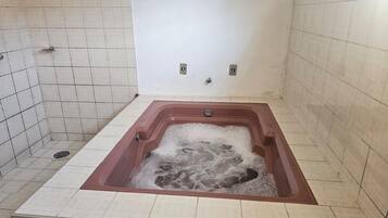 Un baño con una bañera grande llena de agua, paredes con azulejos y una zona de ducha.