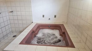 Een badkamer met een groot bad vol water, betegelde wanden en een douchegedeelte.